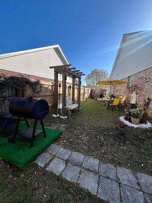A backyard with a barbecue grill, outdoor seating, and a pergola. - Cozy and relaxing beach house, Our Little Pearl in Foley. (Foley)