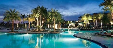 A swimming pool with palm trees and lounge chairs, surrounded by buildings.