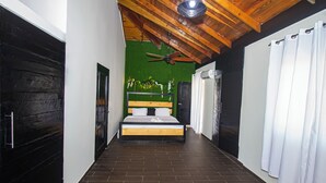 Ein schmaler Flur, der zu einem Schlafzimmer mit einem Bett, einem Deckenventilator und einer grünen Wand führt.