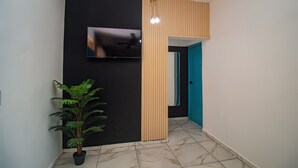 A hallway with a TV mounted on the wall, a potted plant, a wooden panel, and a blue door. - Private pool ,  2 bedroom boho villa (Juan Dolio)