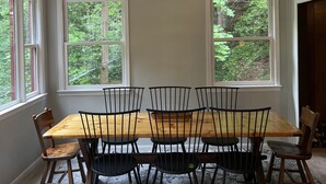 Un espace repas avec une table et des chaises en bois, un lustre moderne et de grandes fenêtres donnant sur un paysage verdoyant.