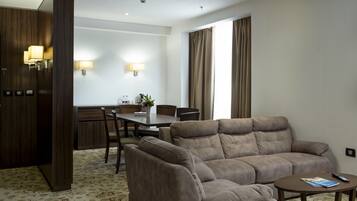 A modern hotel room with a sofa set, a dining table, and a kitchen area.