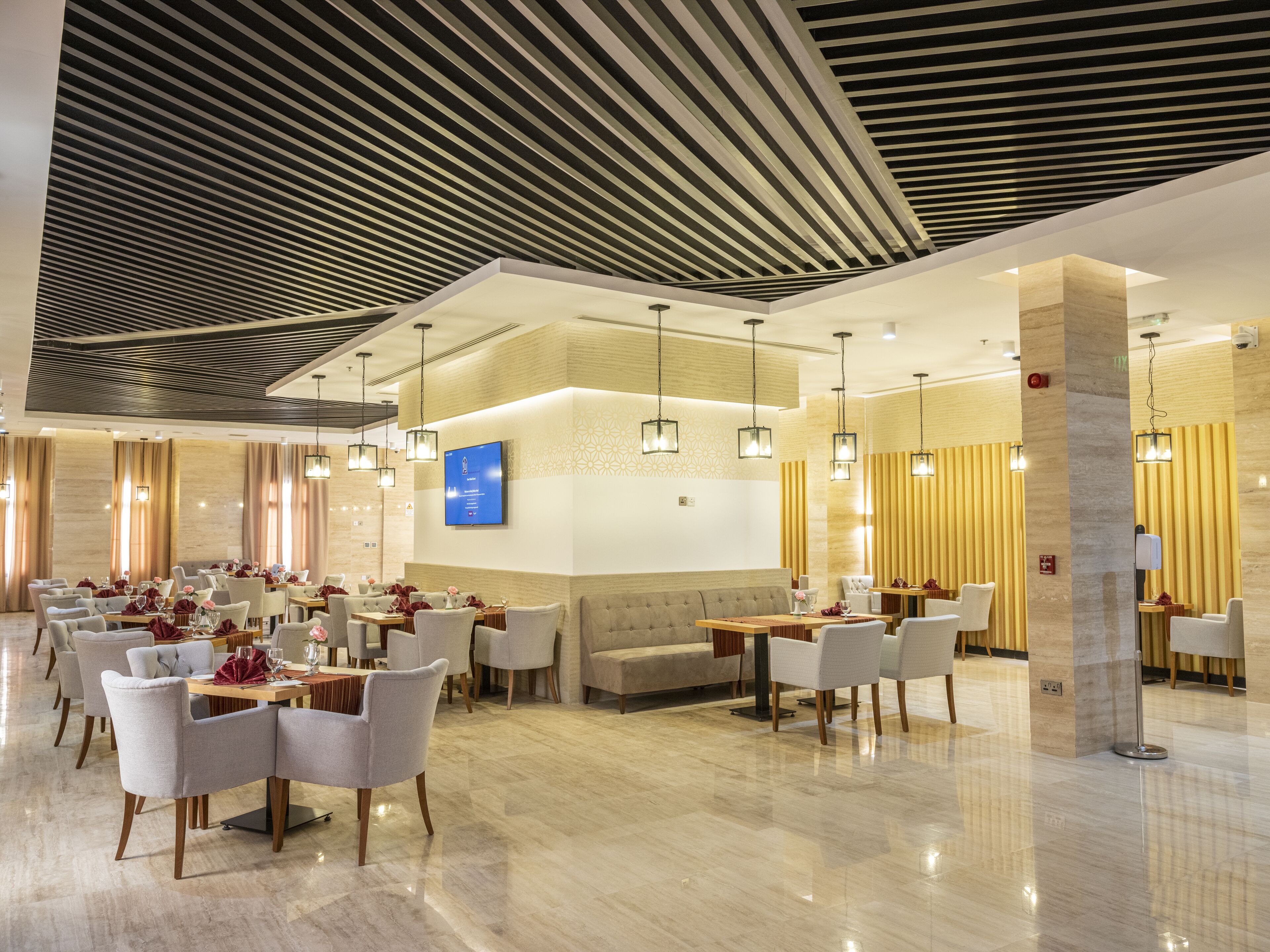 A modern hotel lobby with a spacious seating area, a reception desk, and a flat-screen TV mounted on the wall.