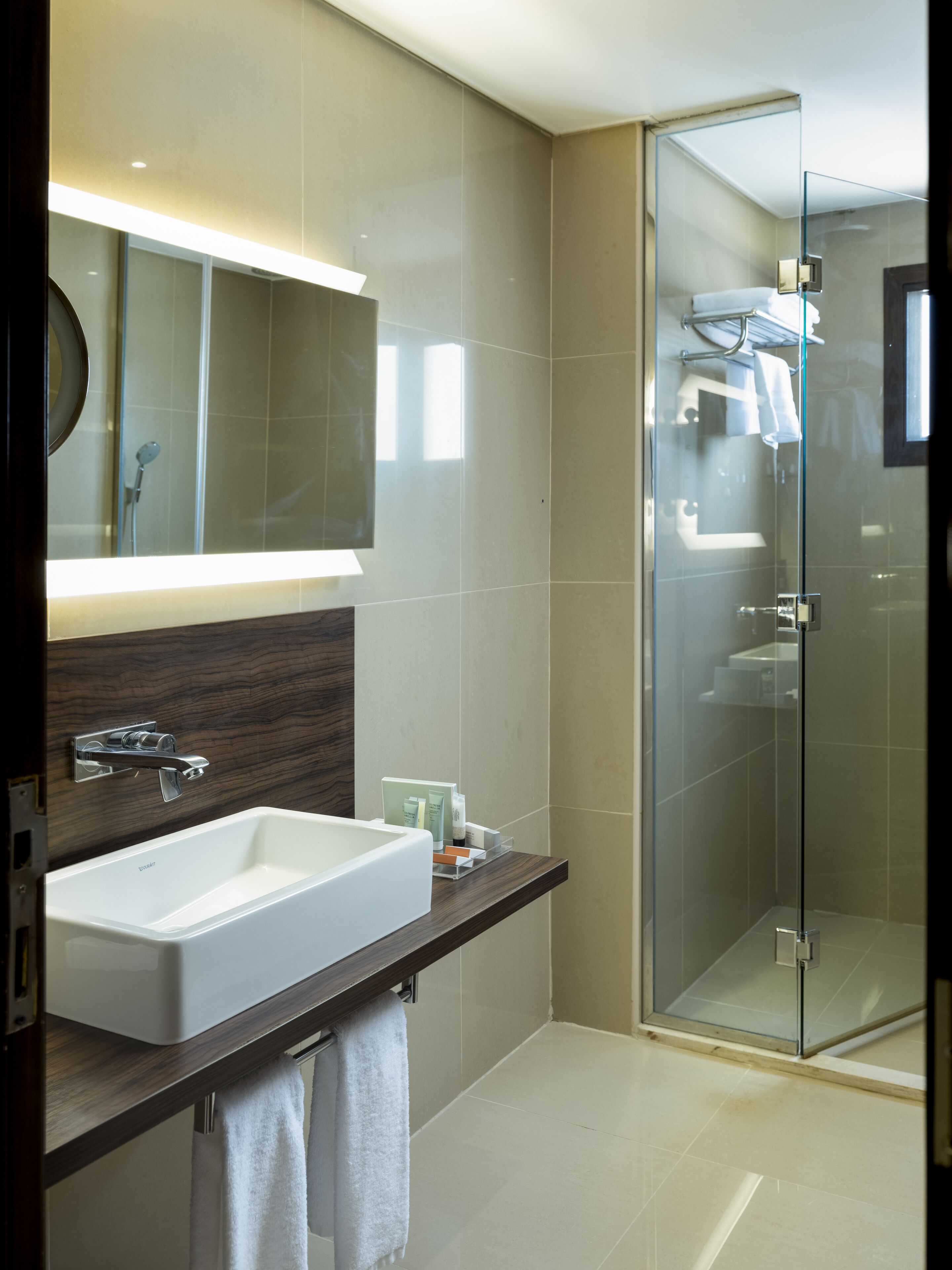 A modern bathroom with a large mirror, a white sink, and a glass-enclosed shower.