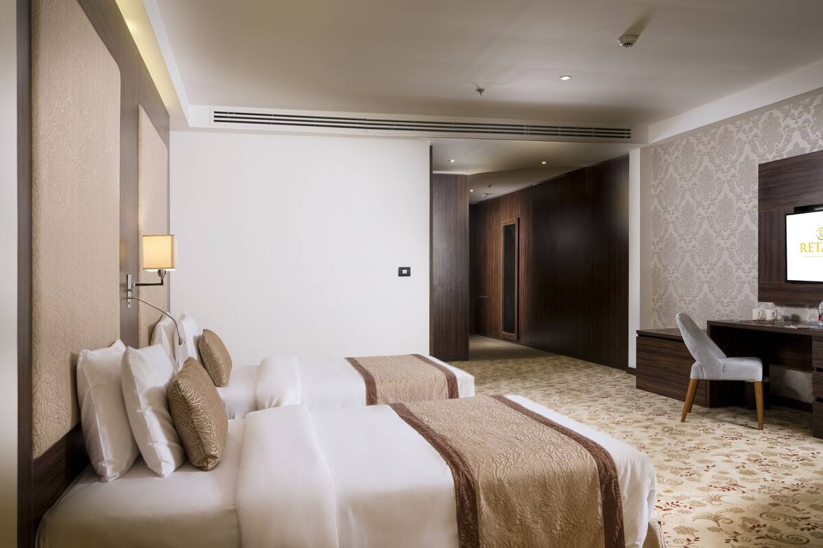 Quarto de hotel com uma cama grande, uma escrivaninha e uma televisão.
