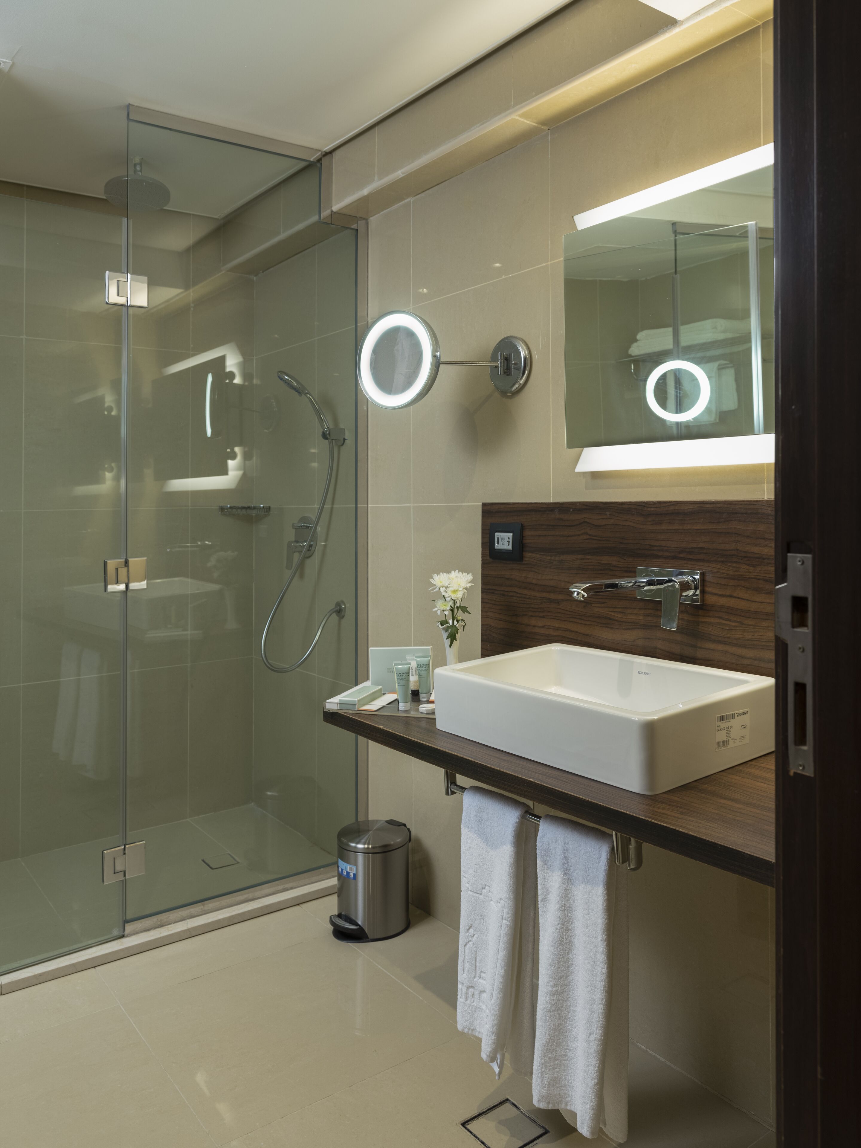 A modern bathroom with a glass-enclosed shower, a vanity with a large mirror, and a sink.