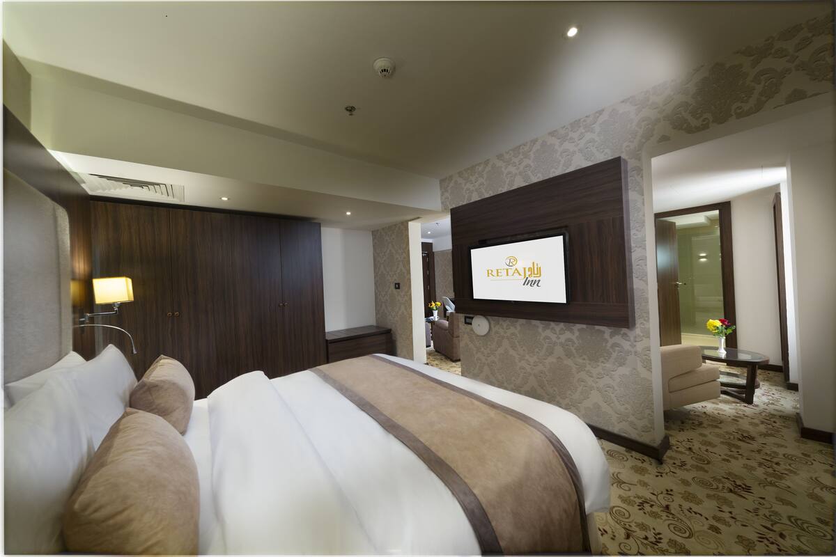 Quarto de hotel com uma cama grande, televisão fixada na parede e relógio de parede.