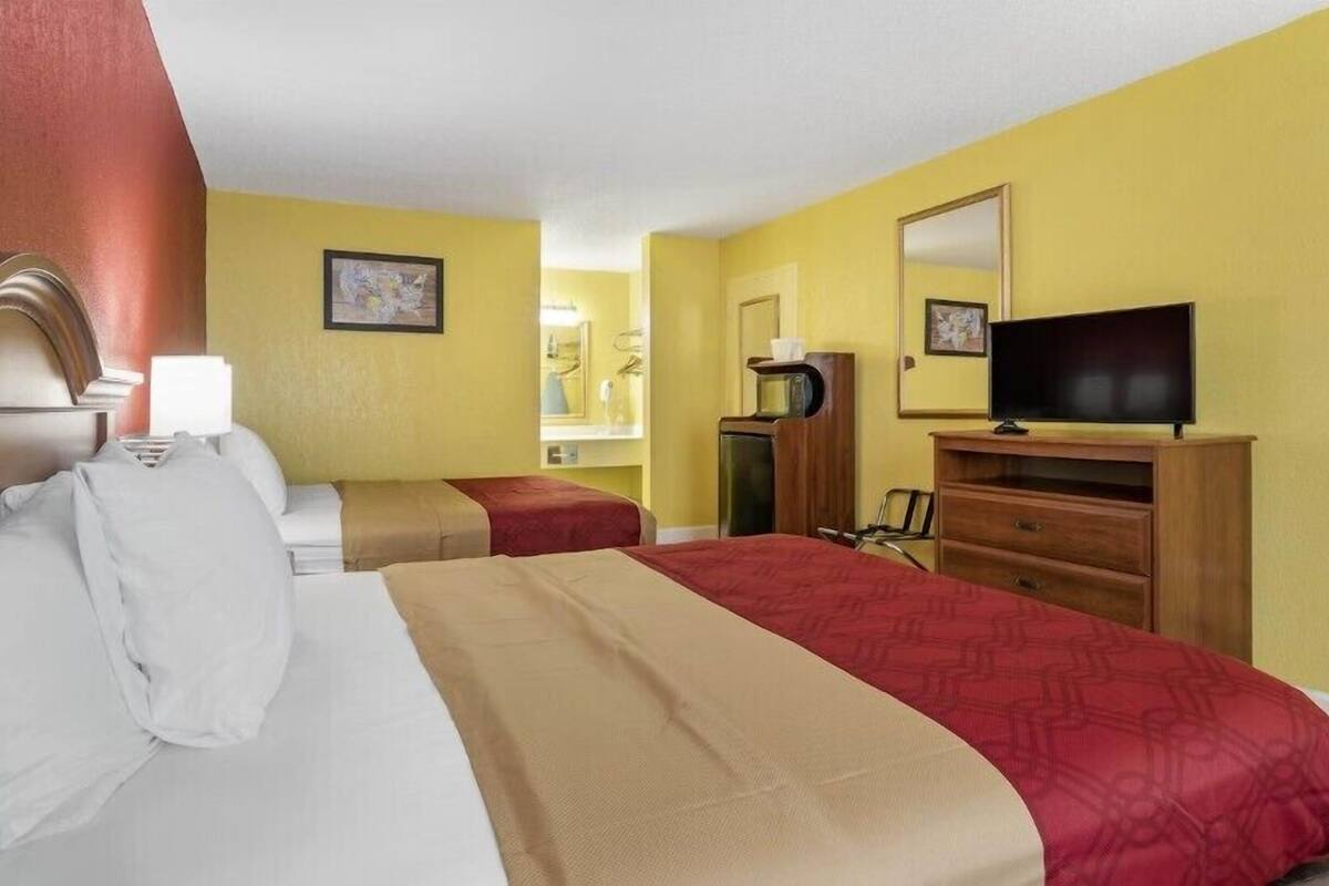 A hotel room with two beds, a TV, a dresser, and a mirror.