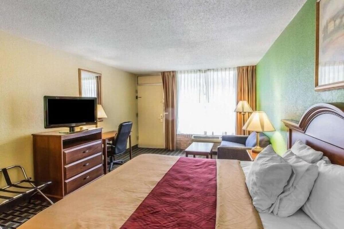 A hotel room with a bed, a desk, a chair, a television, and a window with curtains.