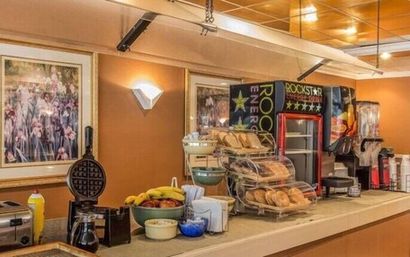 A breakfast bar with a waffle iron, toaster, and various breakfast items like bananas and bread. There are framed pictures on the wall and a Rockstar Energy Drink sign.