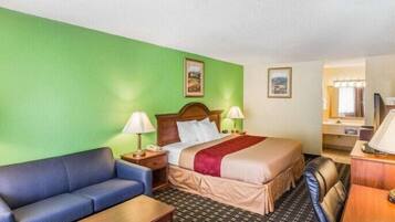 A hotel room with a bed, a blue sofa, a wooden table, and a desk with a chair.