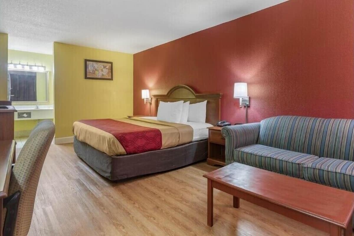 A hotel room with a bed, a sofa, a small table, and a desk with a lamp.