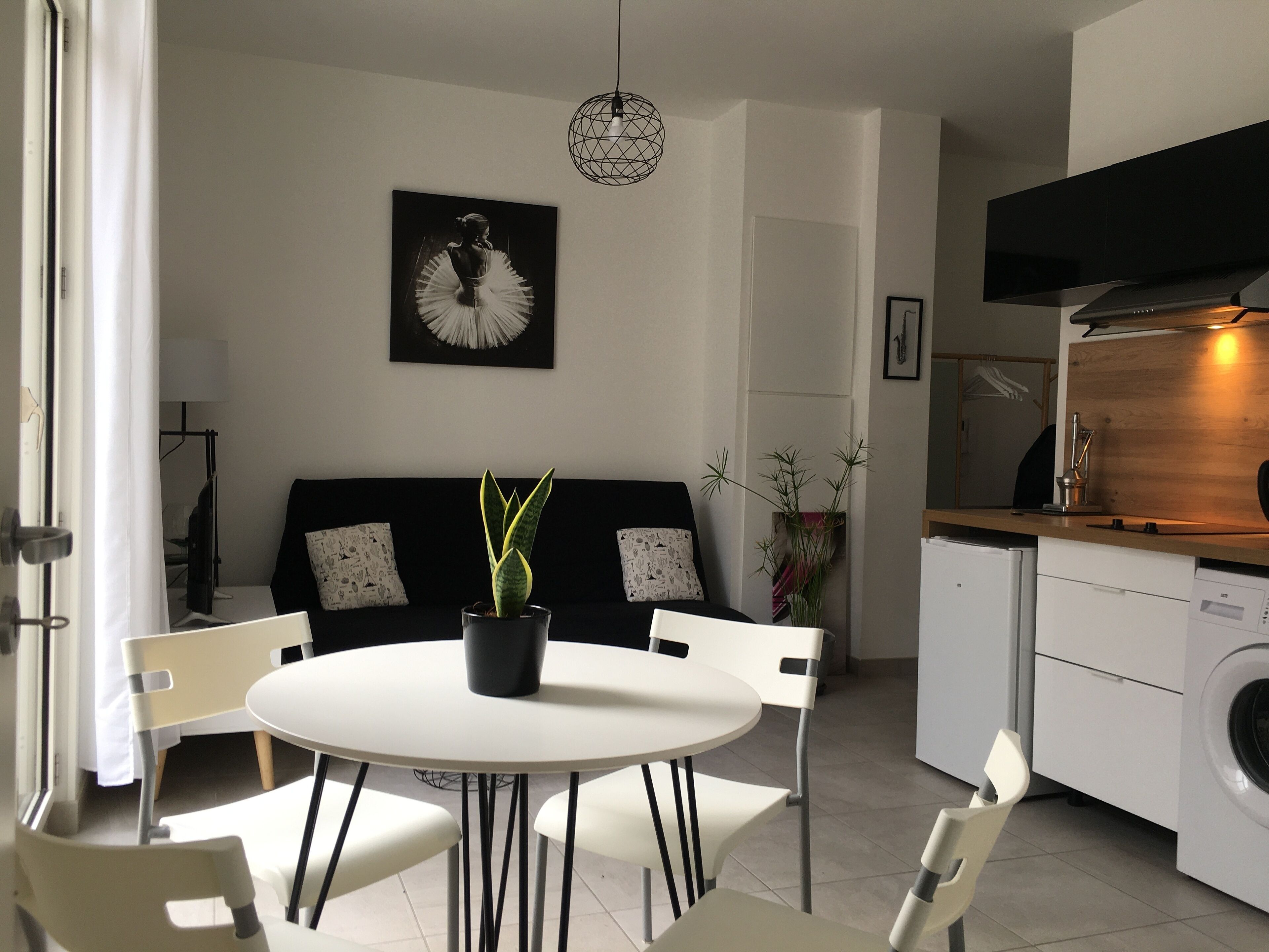 Moderni keittiö, jossa on sisäänrakennettu uuni ja pesukone. Keittiössä on ruokailutila, jossa on pyöreä pöytä ja tuolit, ja seinällä on mustavalkoinen taulu.