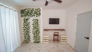 Une chambre d’hôtel avec deux lits, un téléviseur fixé au mur, un ventilateur de plafond et un mur décoré de plantes.
