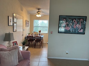 A dining area with a table set for four, a ceiling fan, and a window with blinds.