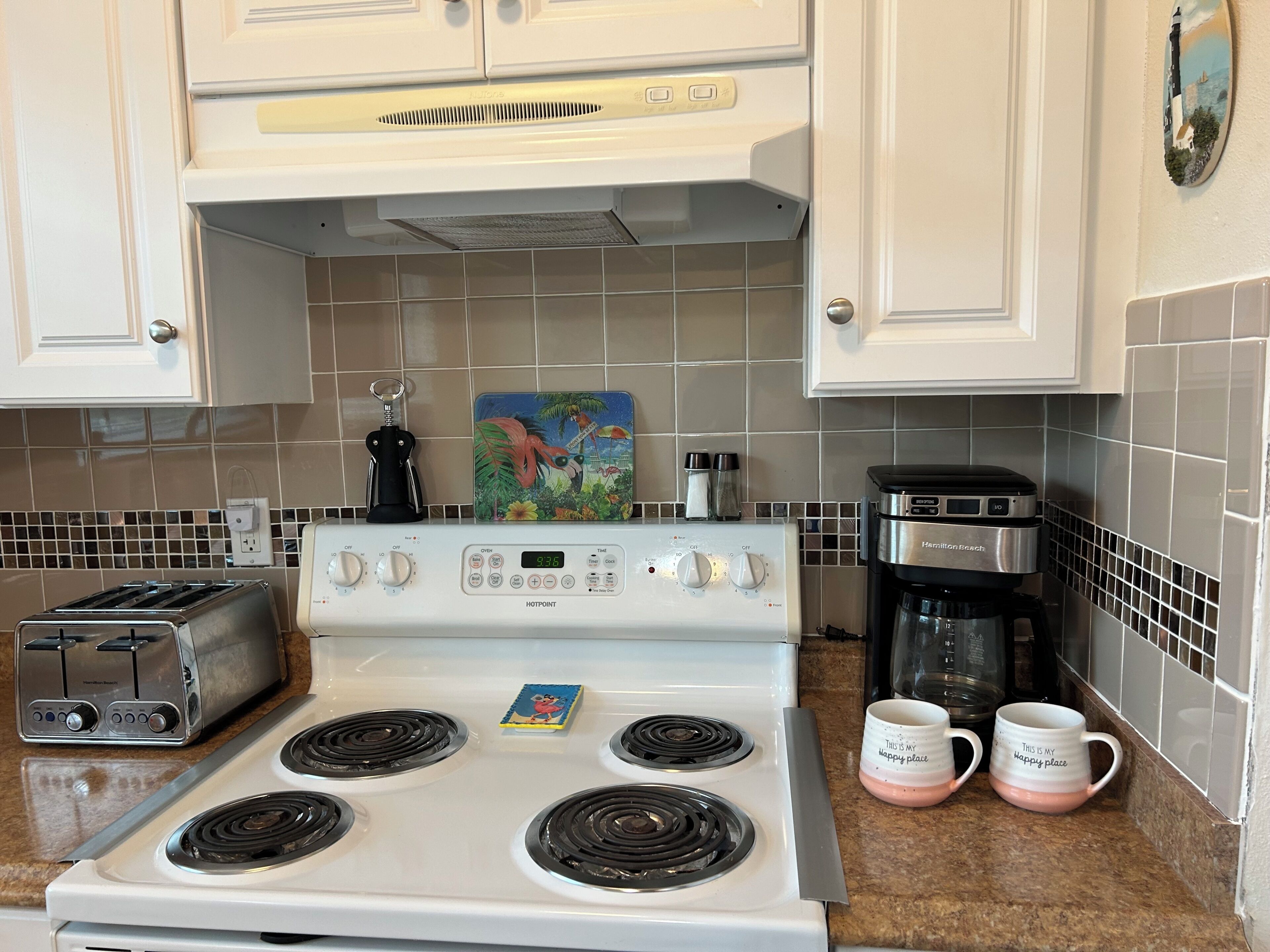 A kitchen with a white stove, a toaster, a coffee maker, and two mugs on the counter.