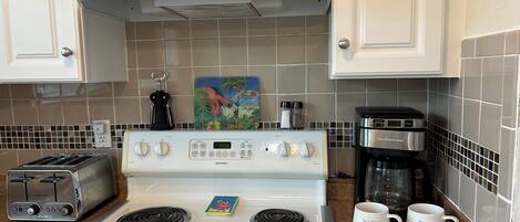 A kitchen with a white stove, a toaster, a coffee maker, and two mugs on the counter.