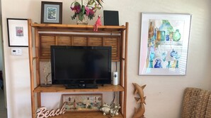 Un meuble de rangement en bois abritant un téléviseur à écran plat, un petit vase blanc et une photographie encadrée représentant des phares.