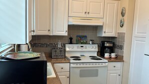 Une cuisine avec des meubles blancs, une cuisinière, une machine à café et un four à micro-ondes.