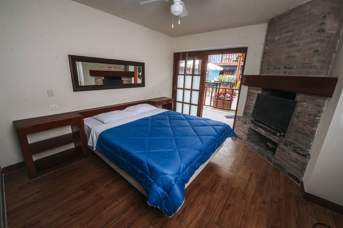 Un dormitorio con cama, cabecera de madera, chimenea y balcón con vistas al exterior.