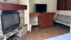 A living room with a fireplace, a television on a wooden stand, a sofa, and a cabinet. - VPX HOTEL & Bungalows (Cieneguilla)