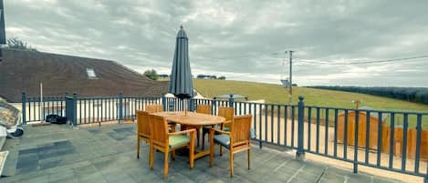 A patio with a table and chairs, a blue umbrella, and a view of a grassy field under a cloudy sky.