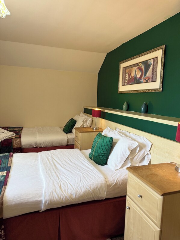 Ein Hotelzimmer mit zwei Betten, einem Nachttisch, einer Kommode, einem Bild an der Wand und einem Regal mit Vasen.