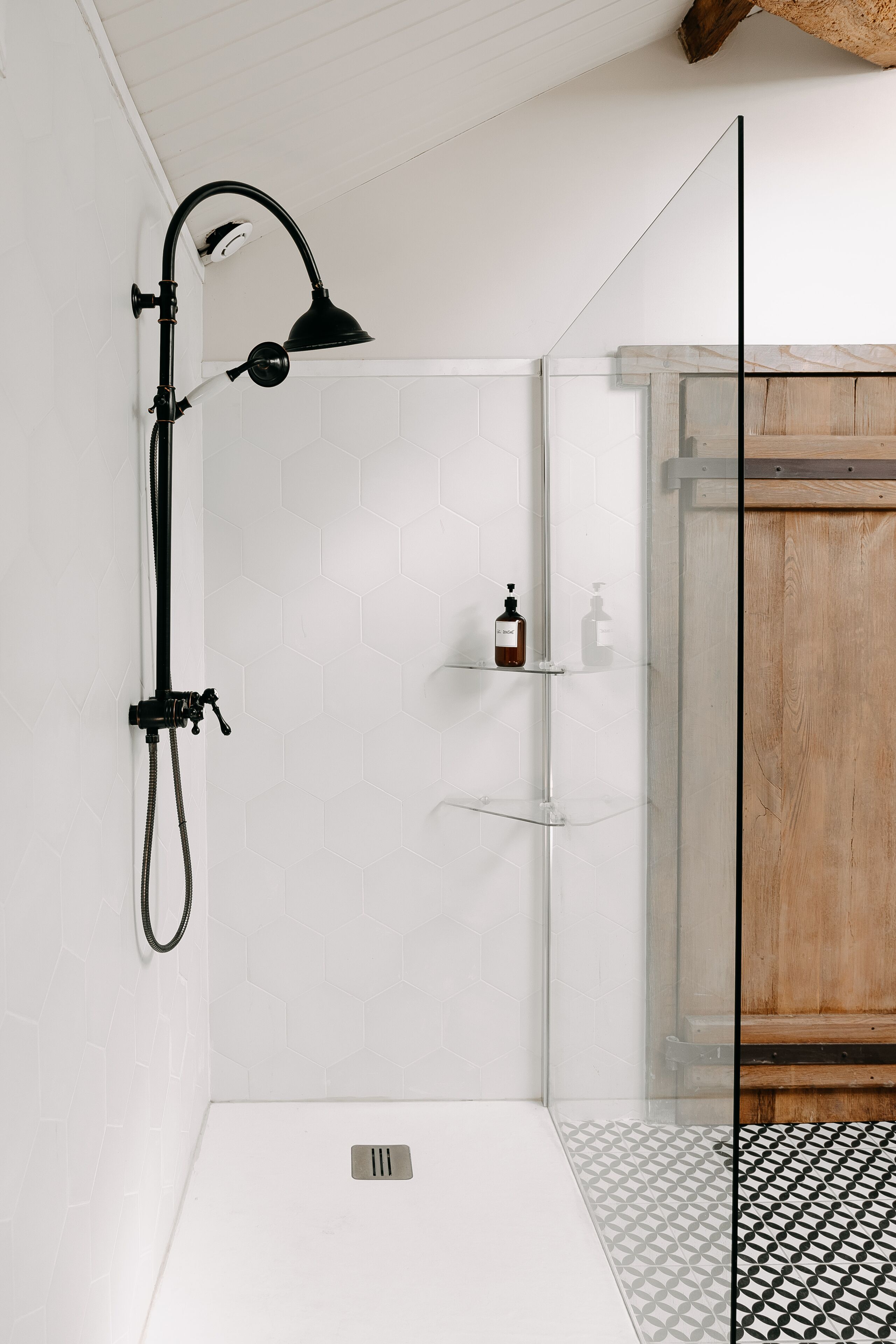 A shower with a glass door, a black handheld showerhead, and a soap dispenser on a shelf.