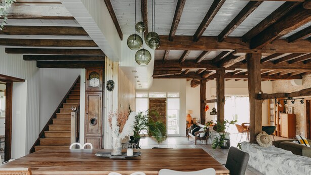 A spacious living area with a wooden dining table, white chairs, a staircase, and a rustic ceiling. - West House (Biaudos)