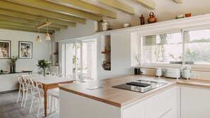A modern kitchen with white cabinetry, a wooden countertop, and a large window providing natural light. - West House (Biaudos)