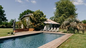 A swimming pool with a wooden deck, surrounded by lounge chairs and a small building with a tiled roof. - West House (Biaudos)