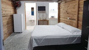 A bedroom with a bed, a small table, a TV, and a refrigerator.