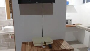 A small kitchen area with a wooden table, a television mounted on the wall, and a sink.