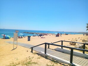 A beach with a wooden walkway leading to the sand, a signpost, and beach umbrellas.