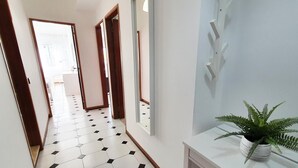 A hallway with a white and black tiled floor, wooden doors, and a white console table with a plant. - T1 Solaris 200m Praia Wifi (Loulé)