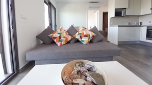 Un salon moderne avec un canapé gris, des coussins aux motifs géométriques et aux couleurs vives, et un bol rempli de pierres décoratives posé sur une table blanche.