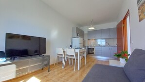 A compact living space with a TV, sofa, dining table, chairs, kitchen area, and a potted plant. - T1 Mira Atlantico 13 A Vista Panor Mica 80M Praia (Loulé)