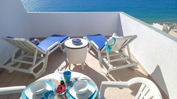 A terrace with white furniture, a table set with plates, bowls, and a glass of water, overlooking the sea. - T1 Mira Atlantico 13 A Vista Panor Mica 80M Praia (Loulé)