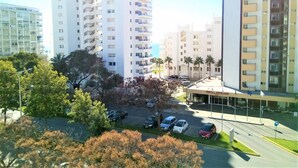 A multi-story hotel with balconies, a parking area, and palm trees. - T1 SOL 200m Praia Vista MAR Wi-fi (Loulé)