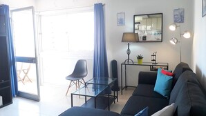 A modern living room with a sofa, a dining table, and a chair. There is a sliding glass door leading to an outdoor area. - T1 SOL 200m Praia Vista MAR Wi-fi (Loulé)