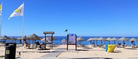 A beach with thatched umbrellas, a signboard, and a trash bin.