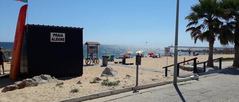 A beach with a black building labeled "PRIA ALEGRE" and a flagpole with a flag.