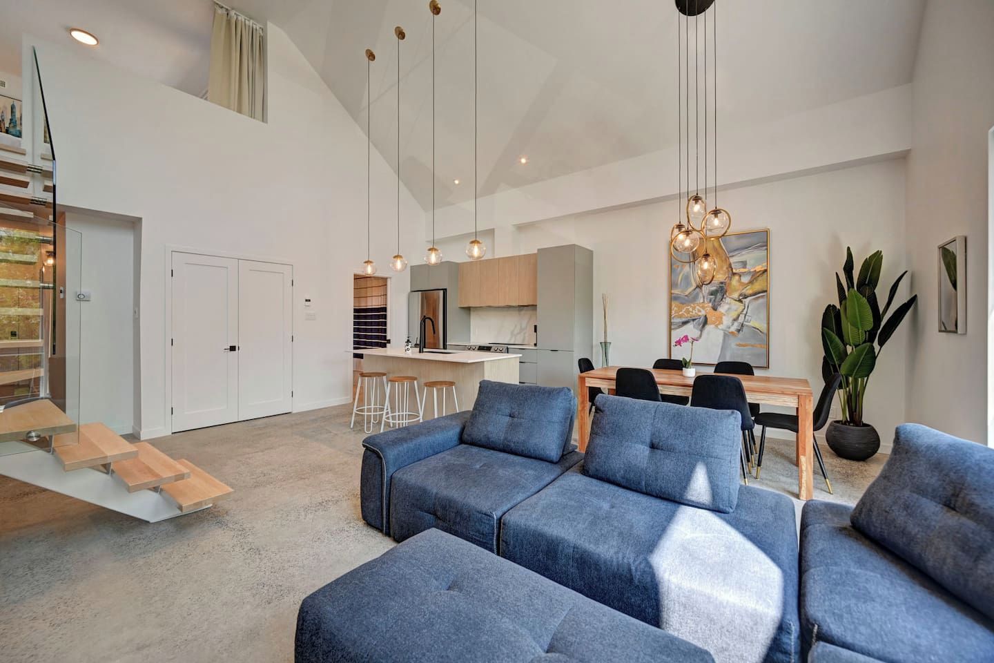 A modern living room with a sectional sofa, a dining area with a wooden table and chairs, and a kitchen in the background.