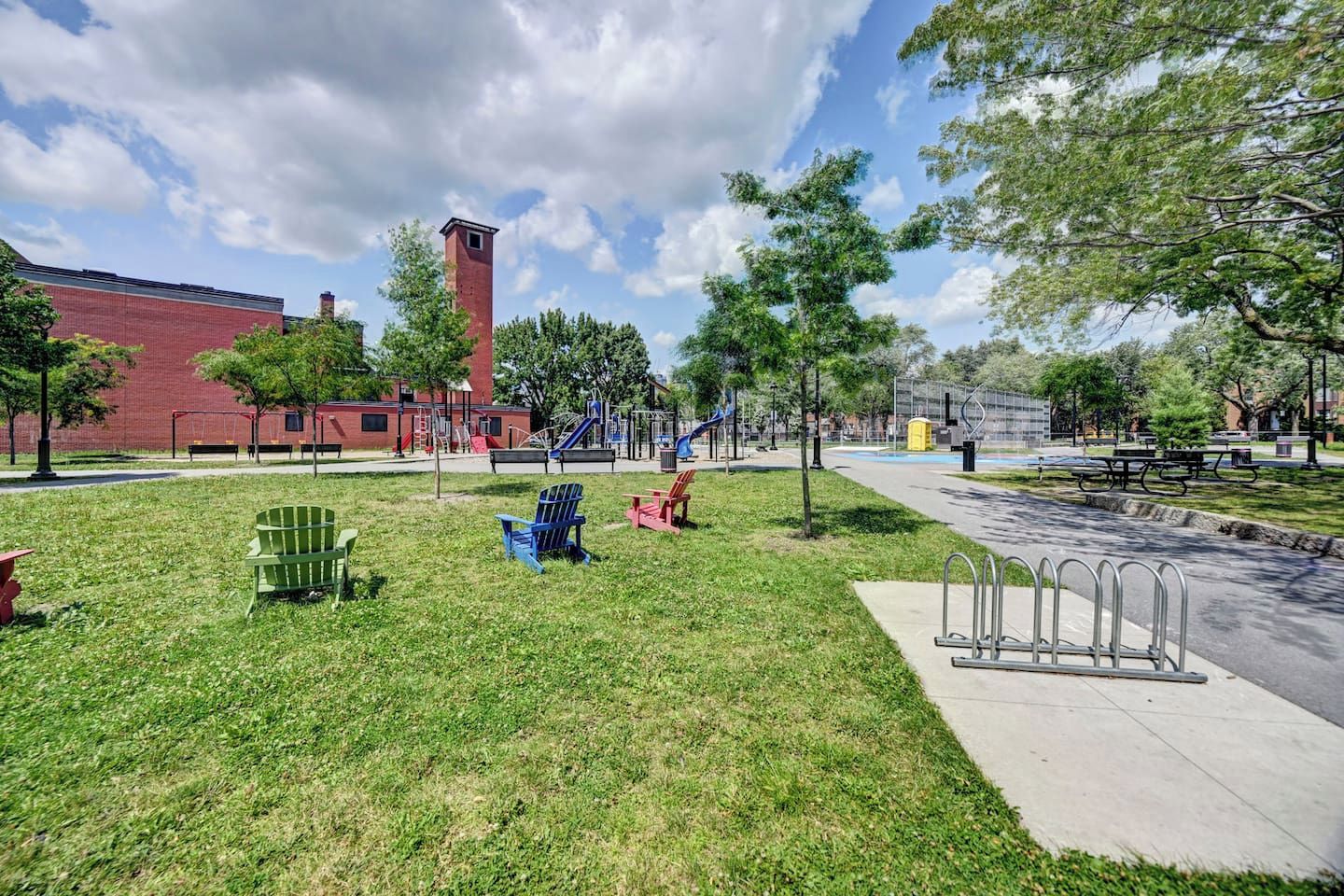 A park with playground equipment, seating areas, and a building in the background.