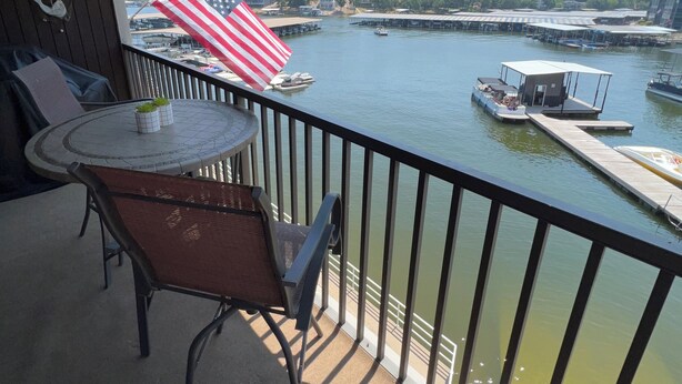 A balcony with a table and chairs, overlooking a marina with boats and an American flag. - Fantastic Water View From Deck  (Osage Beach)