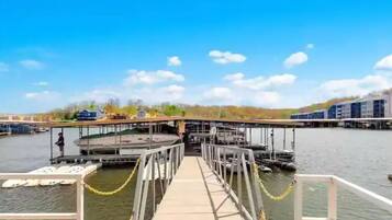 Un muelle con un paseo que conduce a una embarcación, rodeado de agua y edificios al fondo.