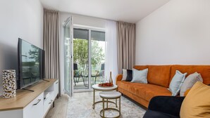Een moderne woonkamer met een bank, televisie en een klein tafeltje met een fles en fruit.