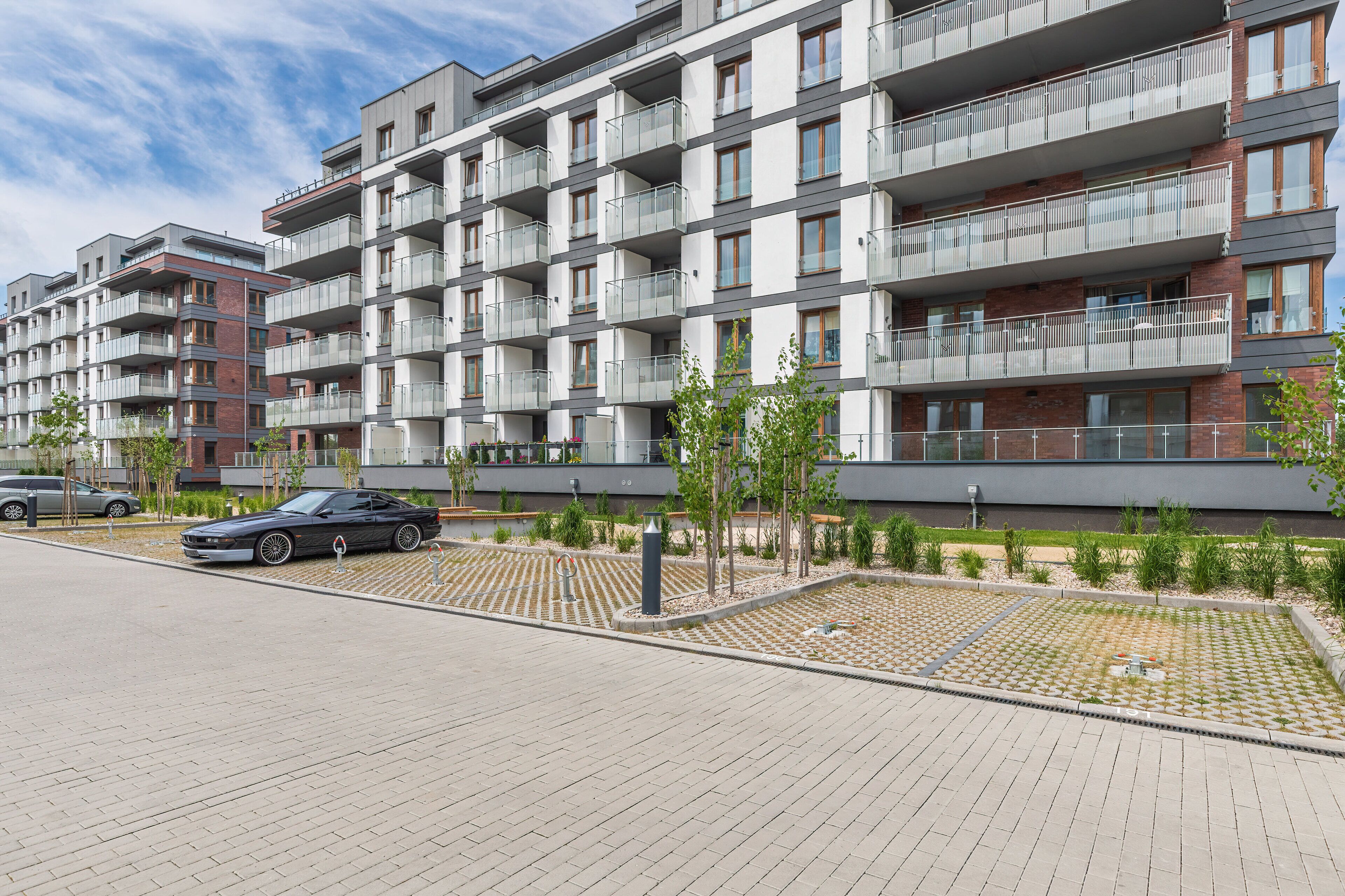 A multi-story residential building with balconies, a paved driveway, and a parked car.