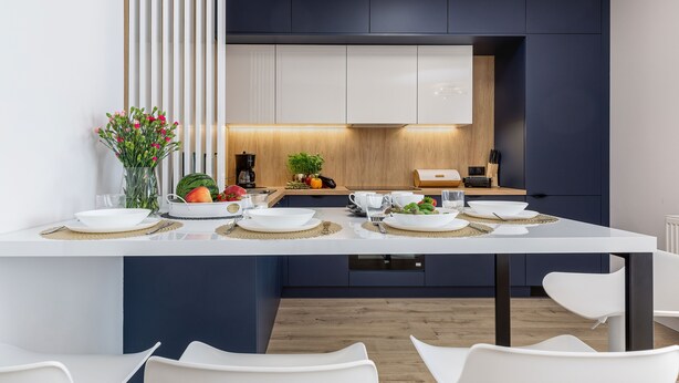 Een moderne keuken met witte kasten, een centraal eiland met een inbouwfornuis, en een eethoek met witte stoelen.