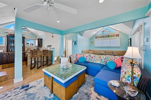 A spacious living room with a blue sofa, a glass coffee table, and a ceiling fan.
